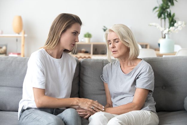 Loving adult daughter talking to sad old mother holding hand