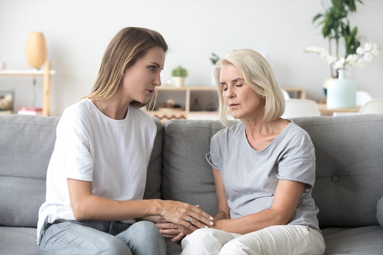 Loving adult daughter talking to sad old mother holding hand