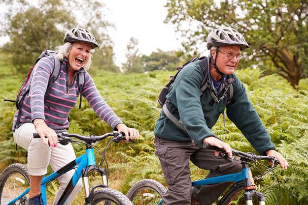 Senior couple riding mountain bikes in the countryside during a camping holiday
