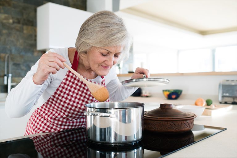 Senior woman in the kitchen cooking, mixing food in a pot
