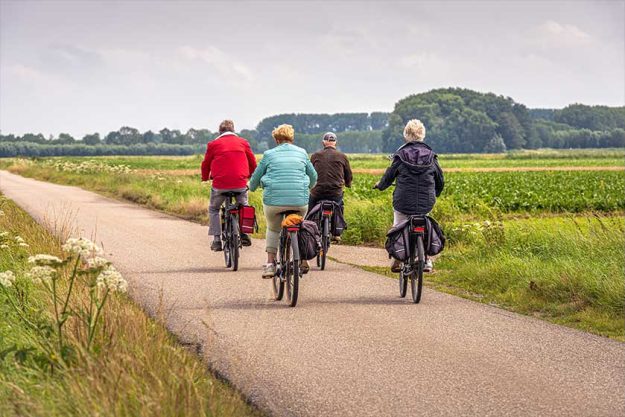 Two elderly unidentified couples with e-bikes cycle on a Dutch country road Two elderly unidentified couples with e-bikes cycle on a Dutch country road