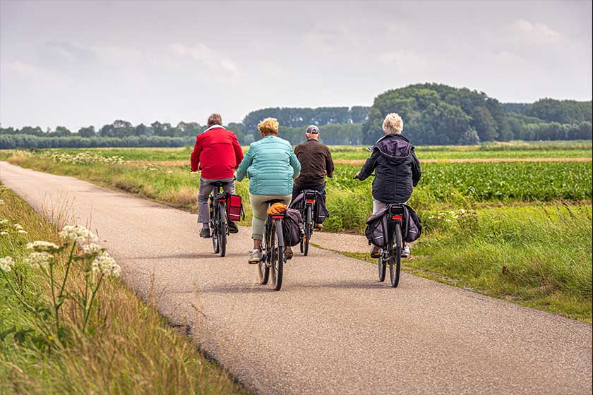Two elderly unidentified couples with e-bikes cycle on a Dutch country road