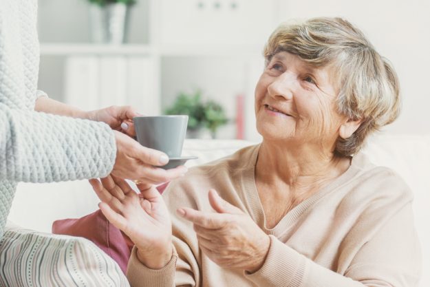 Close-up of person with cup of tea taking care of smiling senior