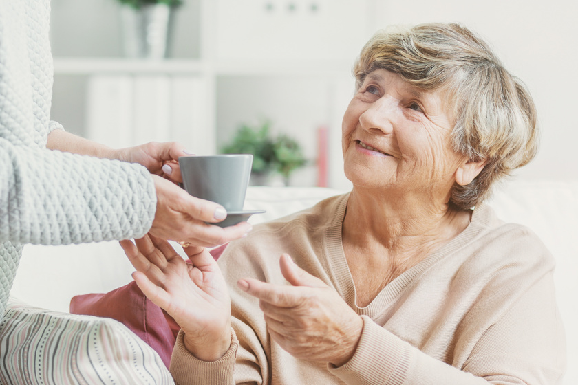 Close-up of person with cup of tea taking care of smiling senior Close-up of person with cup of tea taking care of smiling senior