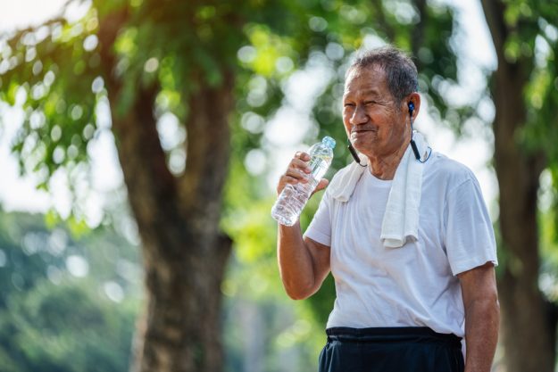 Happy thirsty senior man drinking fresh water after sports in pa