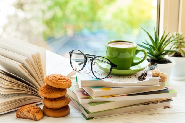 Coffee cup, open book, glasses, cookies and flower on window wit Coffee cup, open book, glasses, cookies and flower on window wit