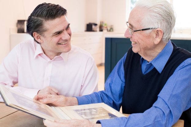 Senior Man Looking At Photo Album With Adult Son 6 Top Benefits Of Living In A Memory Care Community