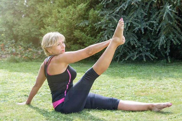 Attractive senior blond woman in single straight leg stretch pose in the garden.