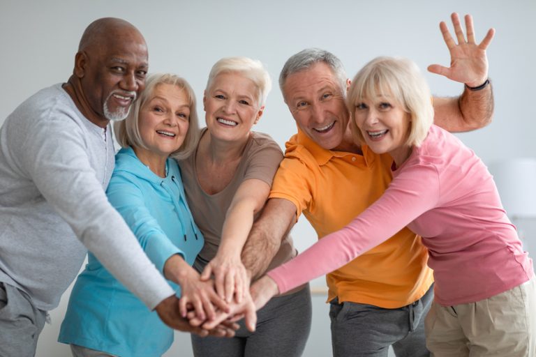 Multiracial group of athletic senior people placing hands Current Retirement Community Trends You Will Love