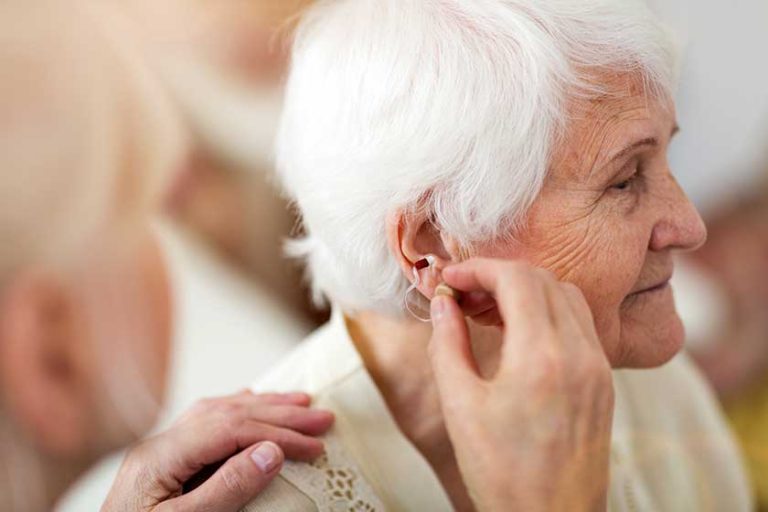 Female doctor applying hearing aid to senior woman’s ear Female doctor applying hearing aid to senior woman's ear