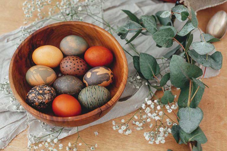 Modern Easter eggs in wooden bowl with spring flowers and eucalyptus on rustic table
