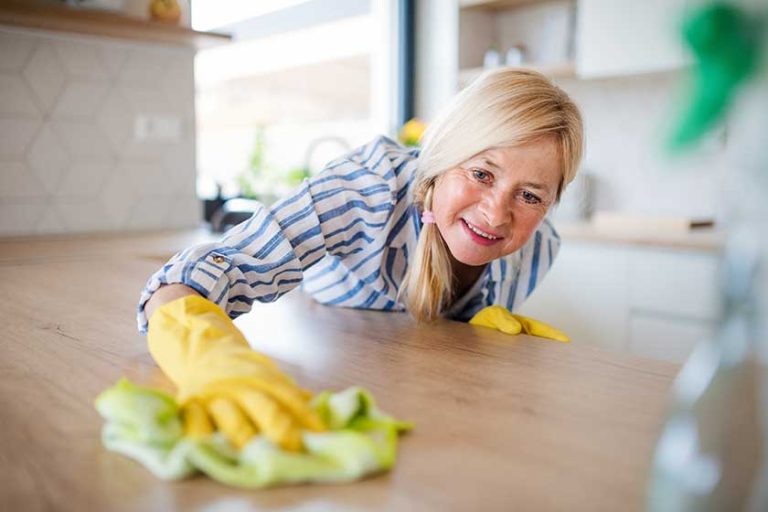 Portrait of senior woman cleaning kitchen counter indoors at home.