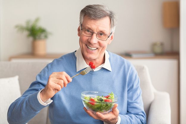Senior Man Eating Vegetable Salad Sitting On Couch