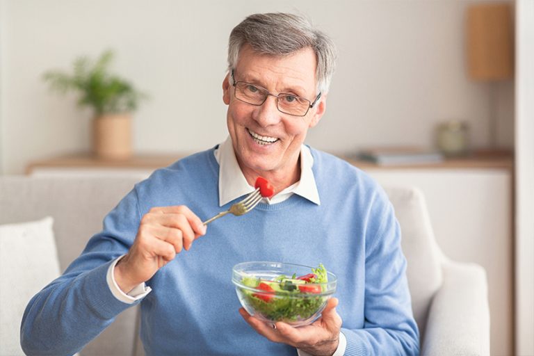 Senior Man Eating Vegetable Salad Sitting On Couch
