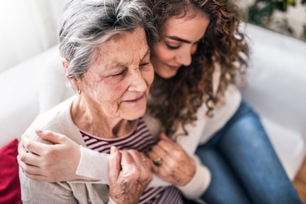 A teenage girl with grandmother at home, hugging.