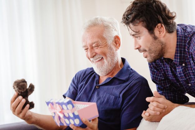 son giving cute teddy gift box to his grand father at Christmas Checking Out The Lutz, FL Memory Care Apartments