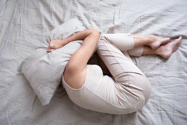 Frightened mature woman lying on bed fetal position covering pillow Frightened mature woman lying on bed fetal position covering pillow