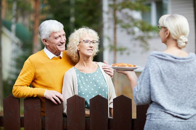 Mature woman giving her new neighbours homemade fresh apple pie on plate over fence