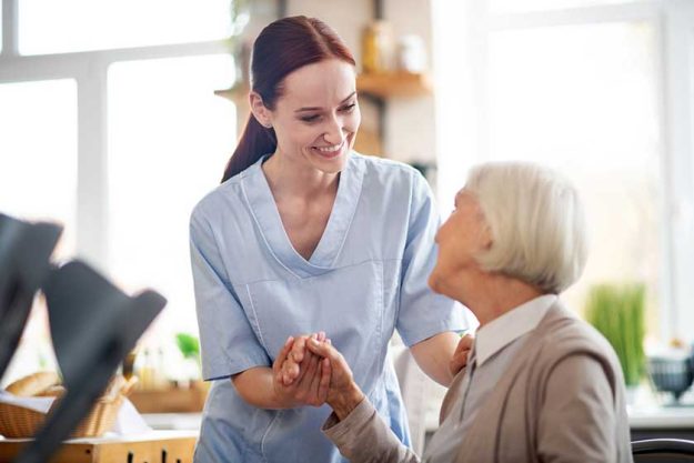Red-haired caregiver smiling and talking to aged woman Red-haired caregiver smiling and talking to aged woman
