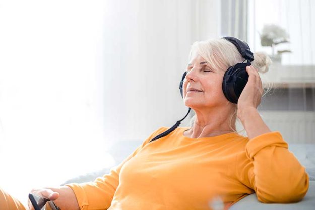 Relaxed senior woman listening her favourite music at home using big headphones