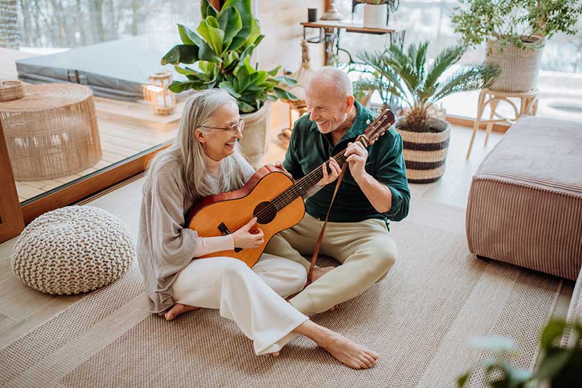 Senior couple playing on guitair, sitting in cozy living room and enjoying autumn day.