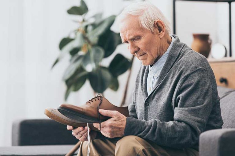 Senior man holding shoes in hands while sitting on sofa