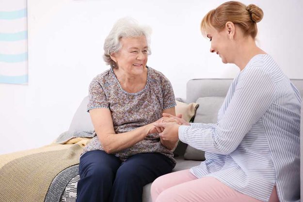 Senior woman and caregiver sitting on sofa at home Senior woman and caregiver sitting on sofa at home