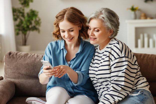 Cheerful mother and daughter using smartphone on sofa 4 Psychological Benefits Of Moving To A Memory Care Community In Norfolk VA