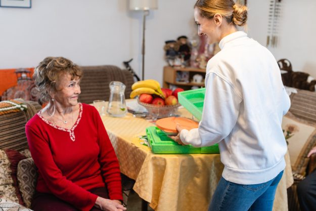 Volunteer serving a meal to senior woman in assisted living program Volunteer serving a meal to senior woman in assisted living program
