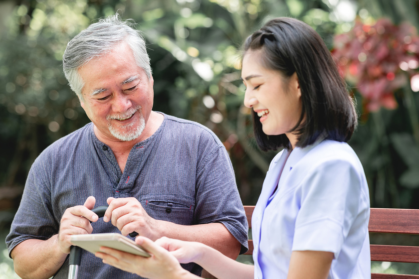 Nurse with patient sitting on bench together looking at tablet.