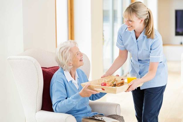 Caregiver giving older woman tray of food