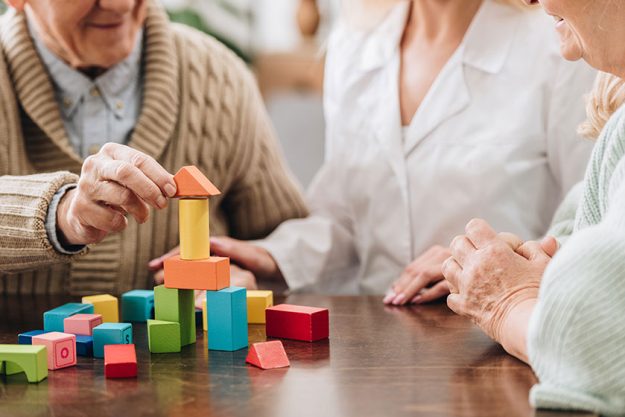 cropped view of caregiver sitting with retired man and woman and playing with wooden toys cropped view of caregiver sitting with retired man and woman and playing with wooden toys