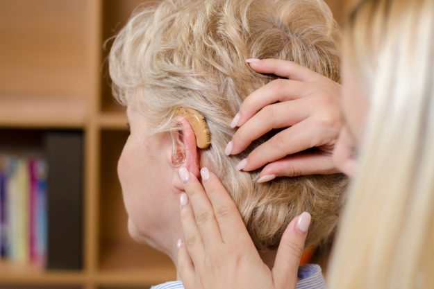 Closeup , back view senior woman having assistance while putting How Memory Care Communities In Keller, TX Help Seniors With Hearing Loss