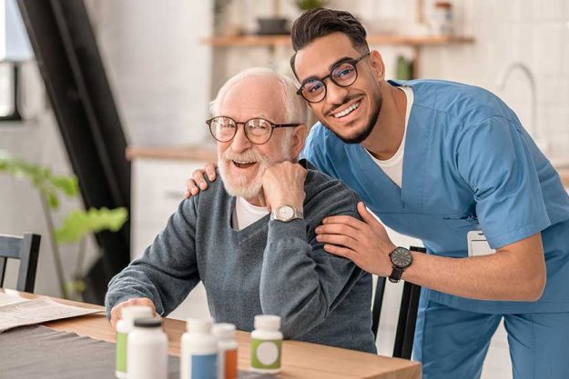 Merry male nurse hugging a pensioner in the kitchen Merry male nurse hugging a pensioner in the kitchen