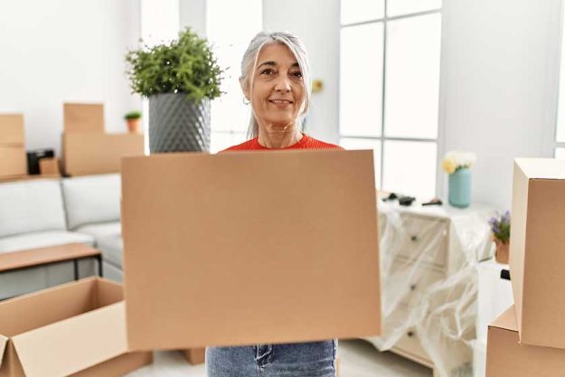 Middle age grey-haired woman smiling confident holding package at new home