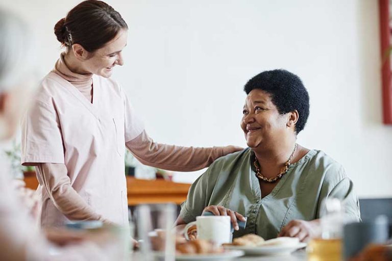 Portrait of smiling young woman caring for senior African-American patient in nursing home