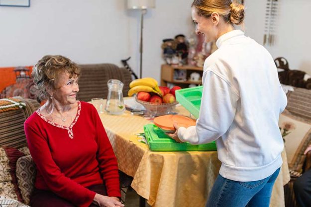 Volunteer serving a meal to senior woman in assisted living program