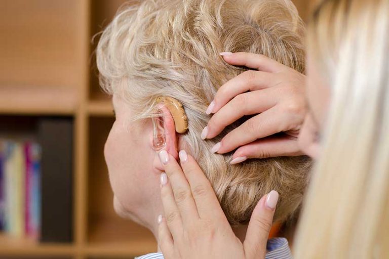Closeup , back view senior woman having assistance while putting hearing aid Closeup , back view senior woman having assistance while putting hearing aid