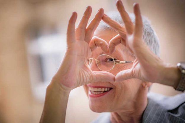 Cute senior old business woman making a heart shape with her hands and fingers Cute senior old business woman making a heart shape with her hands and fingers