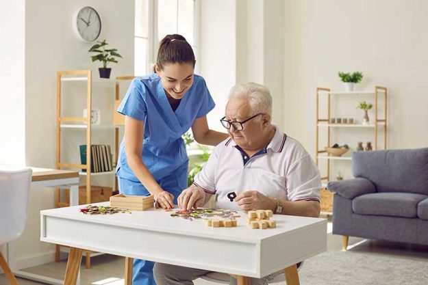 Smiling young female social worker and old man playing with jigsaw puzzle in nursing home Smiling young female social worker and old man playing with jigsaw puzzle in nursing home