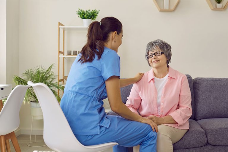 Young pretty nurse at home respectfully communicates with an elderly woman