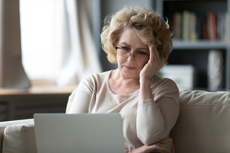 Old woman sit on couch using laptop looks at screen Old woman sit on couch using laptop looks at screen