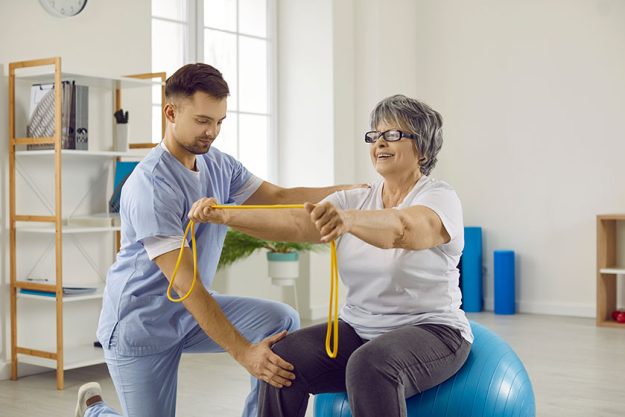 Young doctor at rehabilitation centre helps senior patient do exercises on fit ball Young doctor at rehabilitation centre helps senior patient do exercises on fit ball