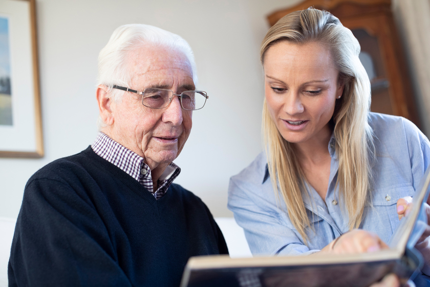 Grandfather Looking At Photo Album With Adult Granddaughter