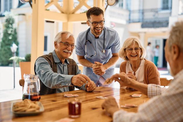 Happy senior friends and male nurse laughing while playing cards Happy senior friends and male nurse laughing while playing cards