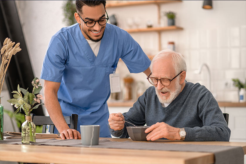 Joyous caregiver watching the pensioner eating breakfast