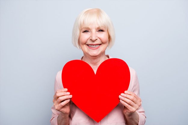 Portrait of old adult blonde caucasian glad lady holding hands big red paper heart shape Portrait of old adult blonde caucasian glad lady holding hands big red paper heart shape