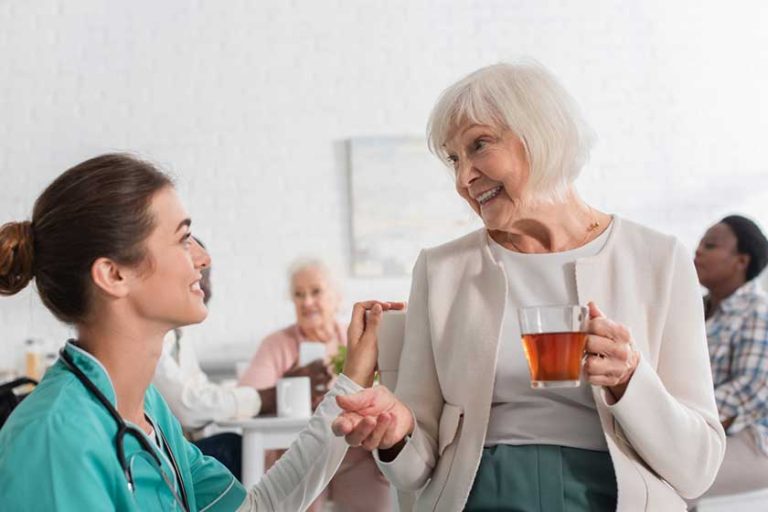 Smiling nurse looking at patient with tea in nursing home Smiling nurse looking at patient with tea in nursing home