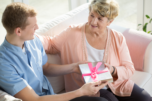 Young nursing assistant gives a present to elderly woman Young nursing assistant gives a present to elderly woman