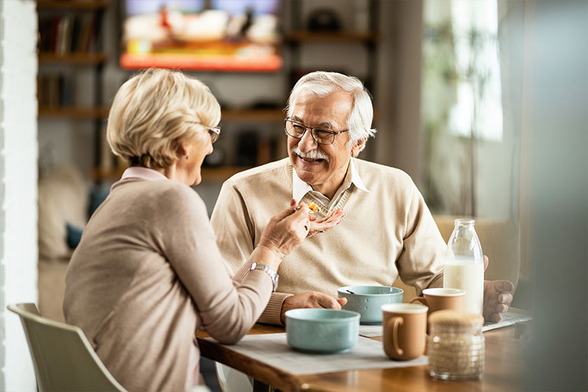 Happy Senior Man Having Fun While Wife Feeding Him Breakfast